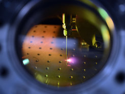Fig. 2: Generation of attosecond laser pulses at the Max Planck Institute of Quantum Optics: A femtosecond laser pulse strikes a cloud of a noble gas emerging from a tiny nozzle. The electrons in the gas atoms absorb the laser energy and subsequently re-emit it in the form of an attosecond pulse.
