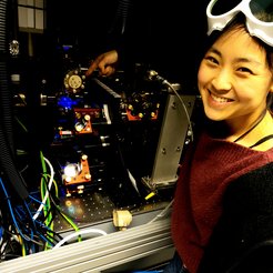 "Siehst du das blaue Licht? Das ist der Laser, den wir benutzen, um Atome bis das Millionstel eines Grades über dem absoluten Nullpunkt herunterzukühlen. Bei solchen Temperaturen zeigen Atome ihre quantenmechanische Natur während sie miteinander interagieren. Wir kontrollieren sie mit mehreren Lasern und können dadurch Materiephasen erzeugen, die wir in der Natur so nicht finden würden. Im Guten wie im Schlechten, diese Maschine beschert uns neue Überraschungen jeden Tag!"