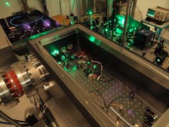 Pulsed enhancement cavity at 515nm before evacuation. Front: Rayleigh scattering makes the very intense intra-cavity beam visible. Back: The power amplifier is recognized by the blue shining fiber.