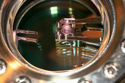 The picture shows a view into one of the vacuum chambers employed in the teleportation experiment. In the center of the vacuum chamber is a mount in which the optical resonator is located. Through the round hole in the center of the mount, the two mirrors of the resonator can be seen (conical white objects).