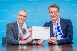 Prof. Immanuel Bloch und Staatsminister Markus Blume halten die Urkunde über die Förderung der Cal-Bay Summer School.